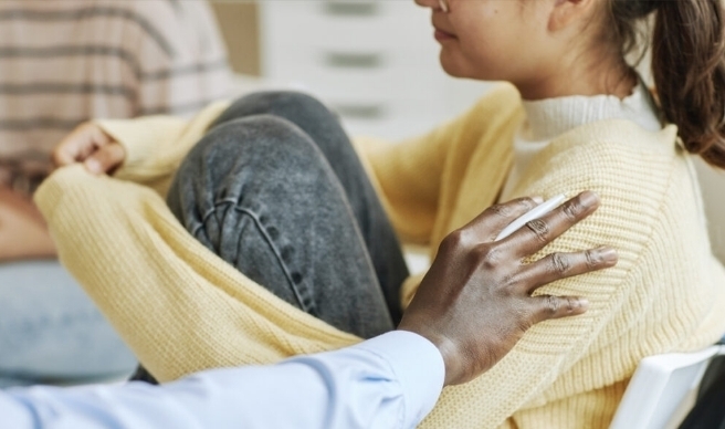 Woman sitting hugging legs while being consoled